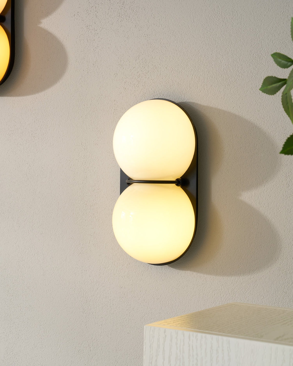 One lit cream Clérachic wall light close up on a pale wall, with another sconce edging into the corner of the frame.