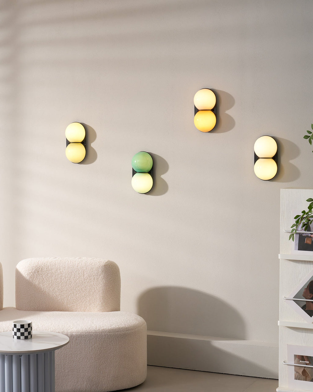 A group of four Clérachic sconces in different colourways on a pale wall above a curved cream sofa and a ribbed side table.