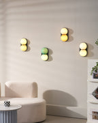 A group of four Clérachic sconces in different colourways on a pale wall above a curved cream sofa and a ribbed side table.