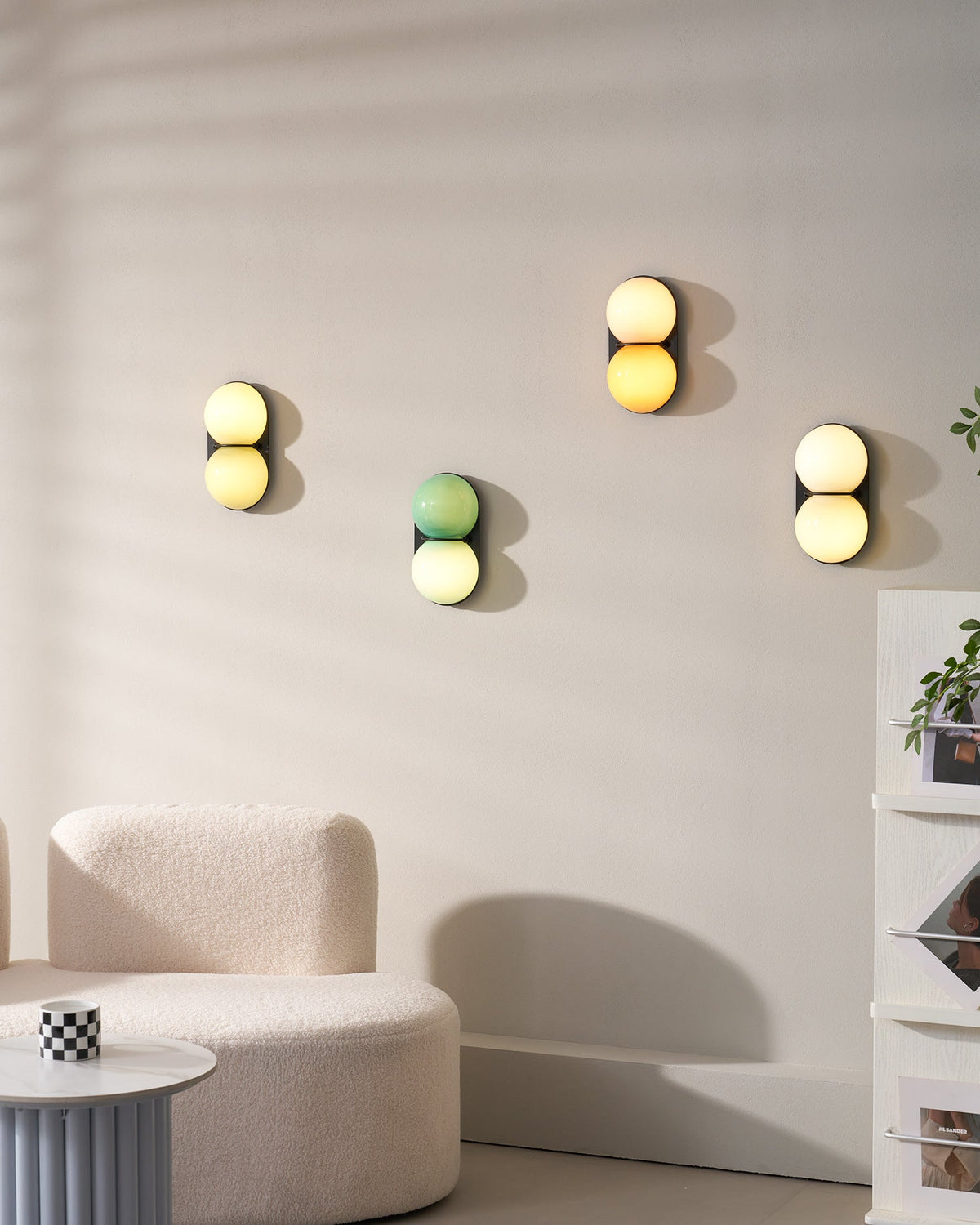 A group of four Clérachic sconces in different colourways on a pale wall above a curved cream sofa and a ribbed side table.