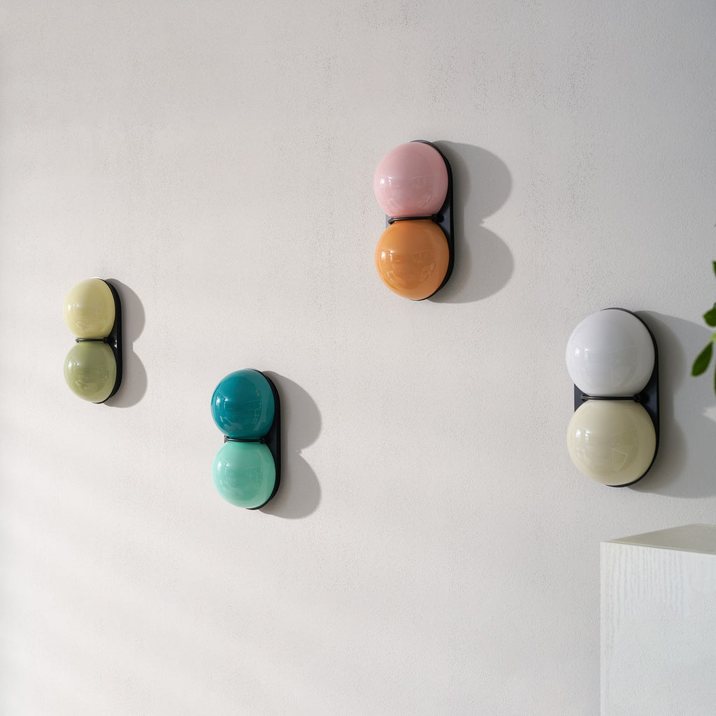 Unlit Clérachic wall lights in olive, teal, pink-orange and grey-white stagger across a white wall near a pale shelf.