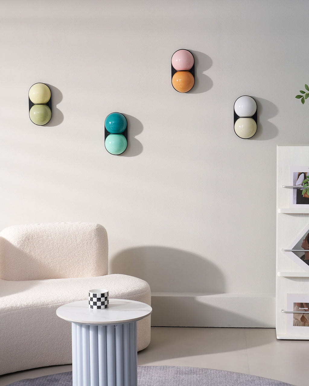 Four Clérachic sconces in assorted colours on a white wall, with a ribbed side table and curved sofa in the corner.