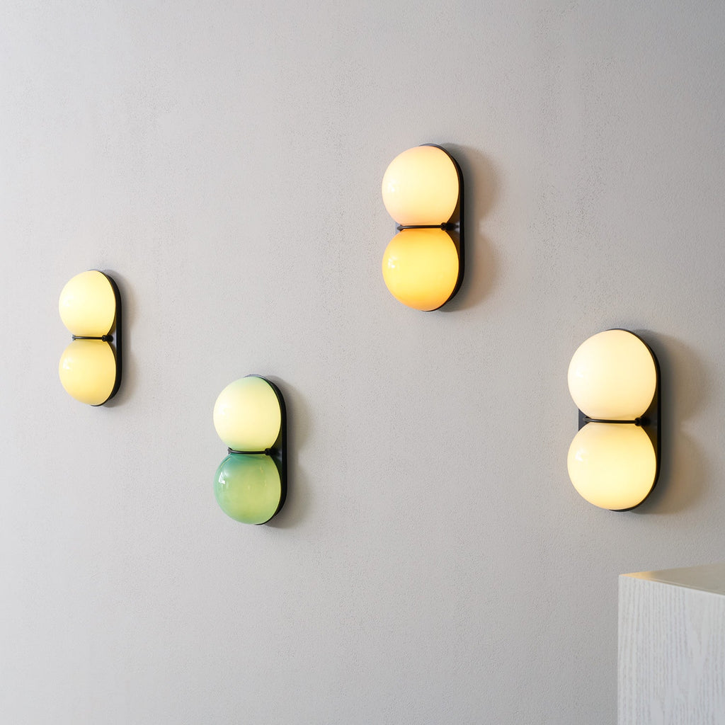 Lit globes in yellow, green-cream, orange-cream and white glow on four Clérachic sconces mounted on a grey wall.