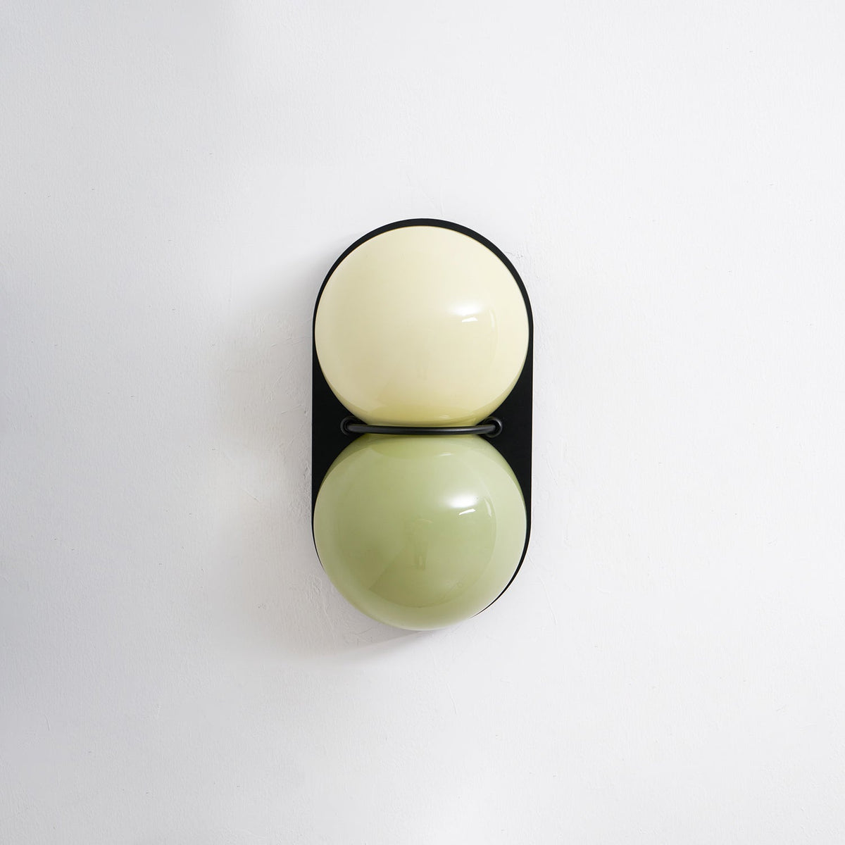 Unlit Clérachic wall light with a cream globe above a sage-green globe, straight on against a plain pale wall.