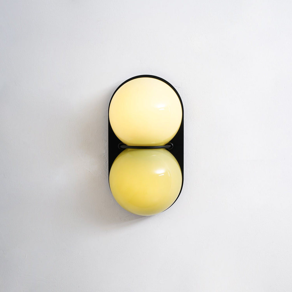Glowing cream above a lemon-yellow globe, this Clérachic wall light is shown straight on its black oval backplate.