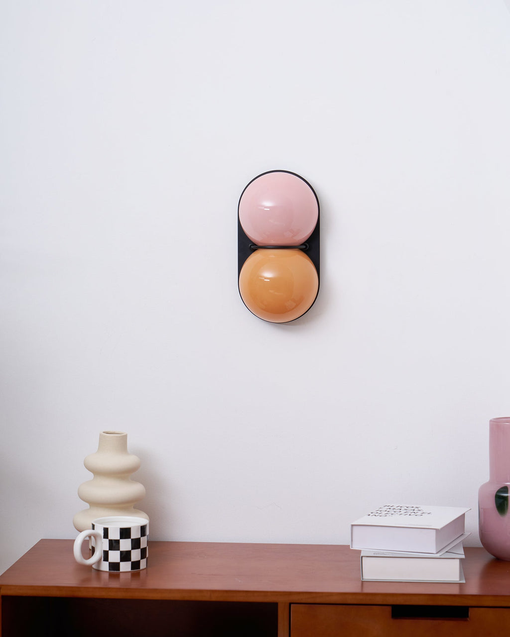 Unlit Clérachic wall light in dusty pink and burnt orange glass above a walnut desk with books and a checked mug.