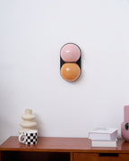Unlit Clérachic wall light in dusty pink and burnt orange glass above a walnut desk with books and a checked mug.