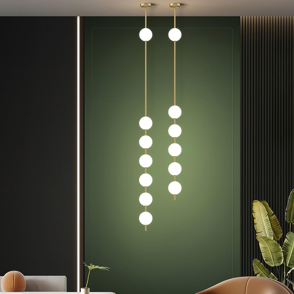 Two tall Clérachic globe pendants, one with six globes and one with five, against a deep green panel in a living room with a rust armchair.