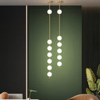 Two tall Clérachic globe pendants, one with six globes and one with five, against a deep green panel in a living room with a rust armchair.