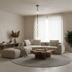 A black-column Clérachic pendant with four globes hung in a cream living room, with sheer curtains, a modular sofa and a round wooden coffee table.