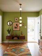 Four-globe Clérachic pendant with a brass column in an entrance hall with olive-green walls, framed prints and a colourful patterned rug.