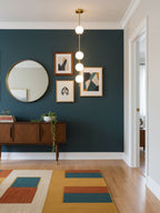 Clérachic pendant with four lit globes on a brass column, hung against a deep teal wall with a round mirror and a walnut sideboard.