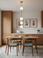 Brass-column Clérachic pendant with four globes in a kitchen, in front of three framed prints above a wooden dining table and teal chairs.