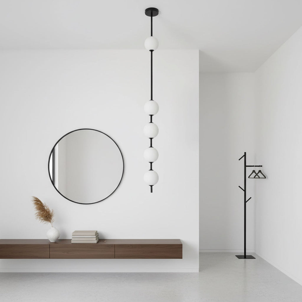 Black-column Clérachic pendant with five white globes beside a round black mirror, a floating wooden shelf and a black coat stand.