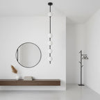Black-column Clérachic pendant with five white globes beside a round black mirror, a floating wooden shelf and a black coat stand.