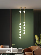 Two long Clérachic pendants lit in a dark green alcove, one with six globes and one with five, above a sofa and a tan armchair.
