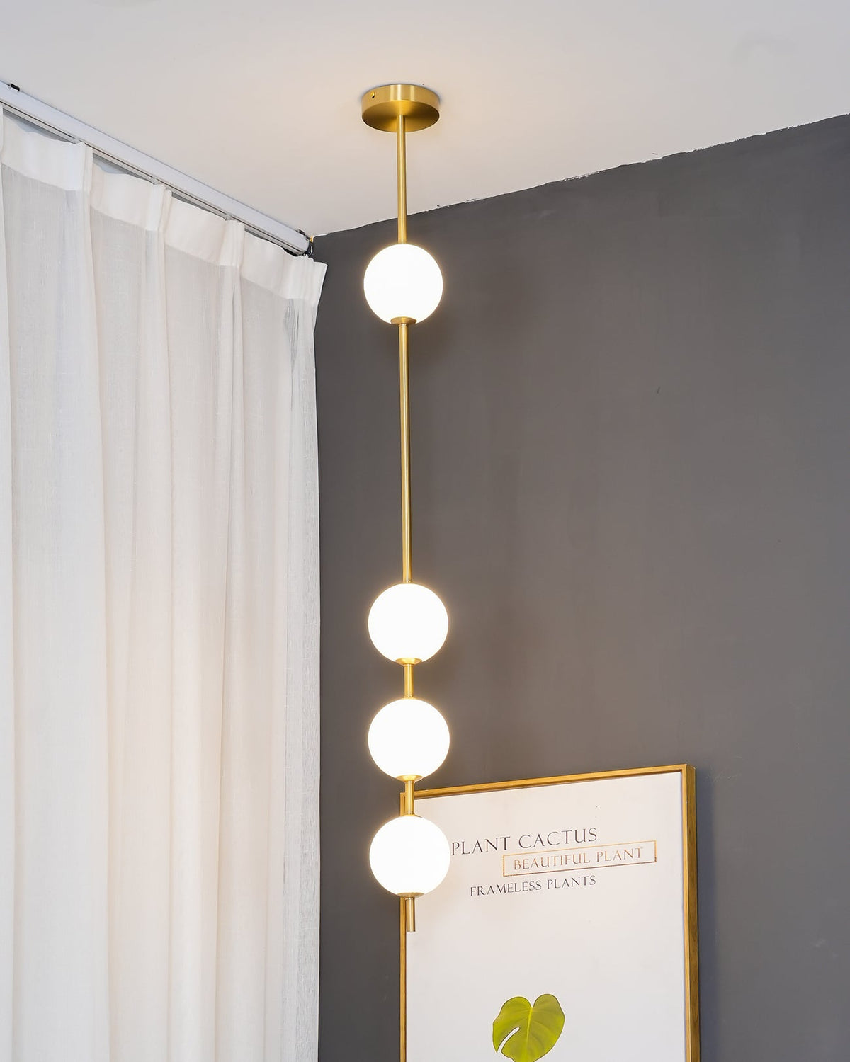 Clérachic pendant with four globes on a brass column, seen up close against a slate-grey wall next to a drawn curtain.