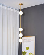 Close, low view of the Clérachic pendant's four opal globes on a brass column, with a curtain rail and a framed print at the edge.