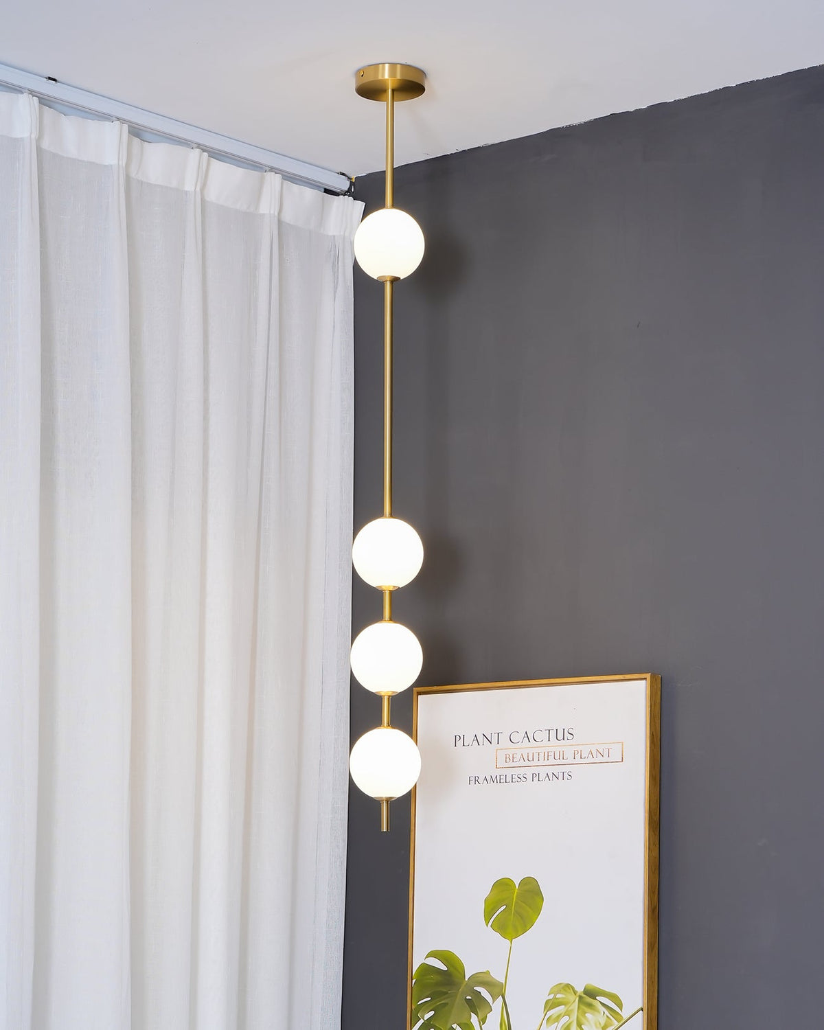 Close, low view of the Clérachic pendant's four opal globes on a brass column, with a curtain rail and a framed print at the edge.