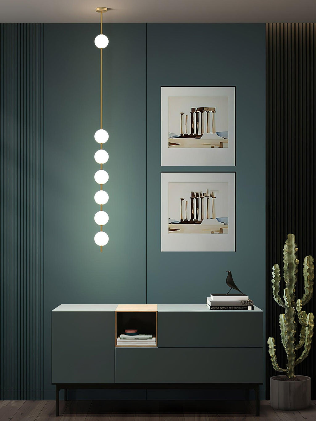 A Clérachic pendant with six lit globes in a dark teal room, above a green sideboard with two framed prints behind it and a cactus beside.