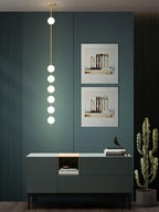 A Clérachic pendant with six lit globes in a dark teal room, above a green sideboard with two framed prints behind it and a cactus beside.