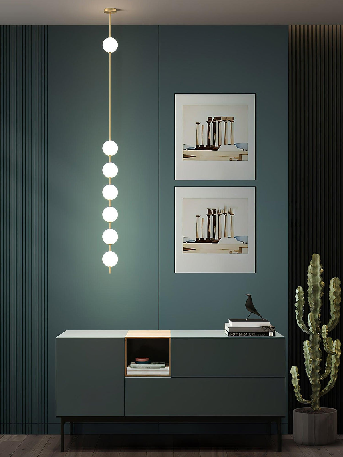 A Clérachic pendant with six lit globes in a dark teal room, above a green sideboard with two framed prints behind it and a cactus beside.