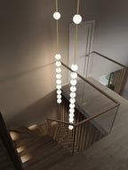 Two long Clérachic globe pendants hanging down a stairwell, seen from above, beside a glass balustrade and a timber staircase.