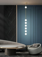 Six-globe Clérachic pendant in a lounge with a blue panelled wall, a dark marble panel and a curved grey sofa.