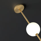 Close view of the round brass ceiling plate, the slim brass rod and one opal glass globe of this Clérachic pendant on a dark background.