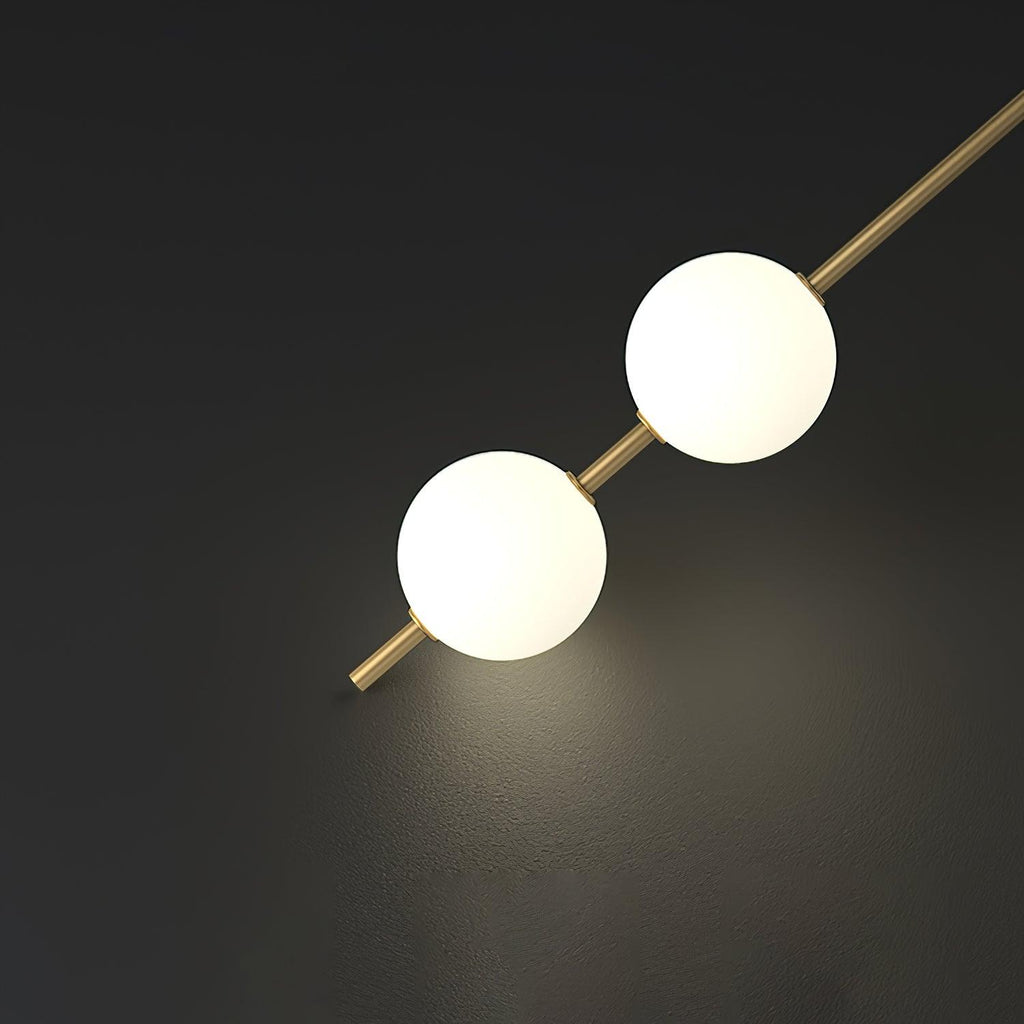 Two opal globes of this Clérachic pendant on a diagonal brass rod, lit against a dark wall with a soft pool of light behind.