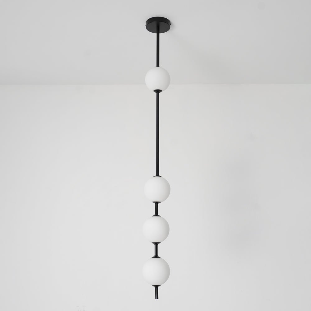 Black-column Clérachic pendant with four opal globes and a black ceiling plate, seen against a white wall with a light floor.