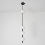 Black-column Clérachic pendant with four opal globes and a black ceiling plate, seen against a white wall with a light floor.