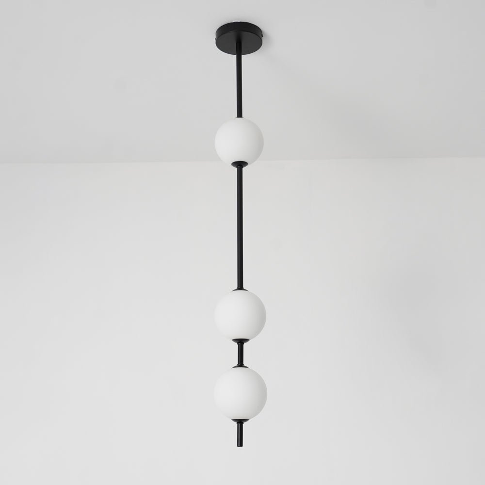 Close view of a black Clérachic column with three opal globes, from the round black ceiling plate down, against a pale wall.