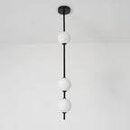 Close view of a black Clérachic column with three opal globes, from the round black ceiling plate down, against a pale wall.