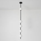 Black-column Clérachic pendant with five opal globes, the top one near a black ceiling plate, in front of a plain white wall.