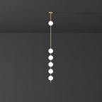 Clérachic pendant with five opal globes lit white on a brass column, against a dark charcoal wall and ceiling.