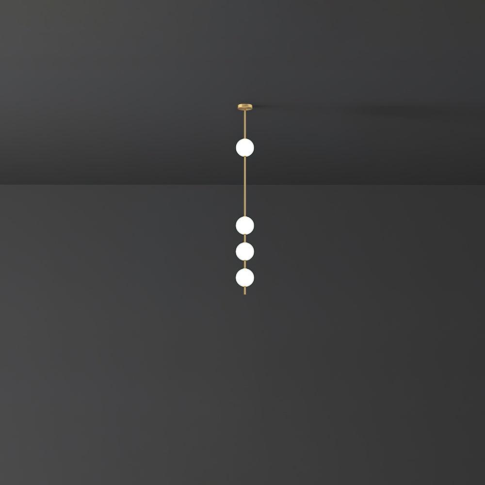 Distant view of a Clérachic pendant with four lit globes on a slim brass column, against a charcoal wall with a lit ceiling edge.