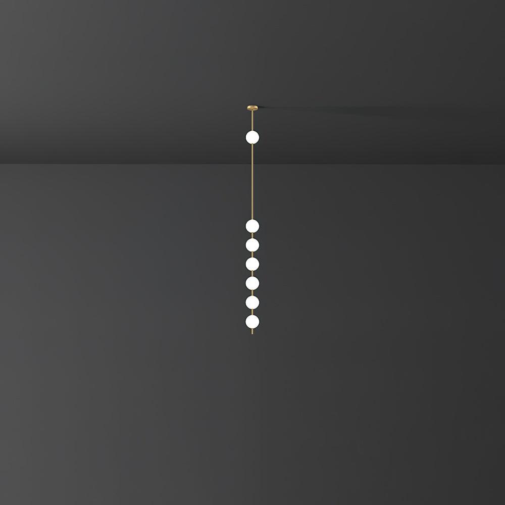 A tall, slender Clérachic pendant with six lit globes on a brass rod, shown far off against a dark grey wall.