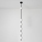 Black-column Clérachic pendant with six opal globes against a white wall, with a black ceiling plate and a light floor.