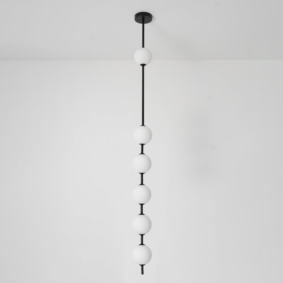 Black-column Clérachic pendant with six opal globes against a white wall, with a black ceiling plate and a light floor.
