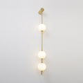 The Clérachic Stacked Globe Wall Sconce in brass, lit, three globes glowing top to bottom against white.