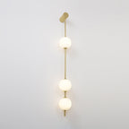 The Clérachic Stacked Globe Wall Sconce in brass, lit, three globes glowing top to bottom against white.