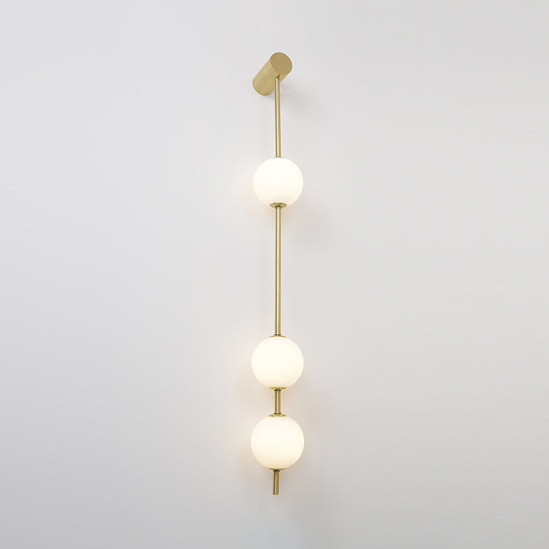 The Clérachic Stacked Globe Wall Sconce in brass, lit, three globes glowing top to bottom against white.