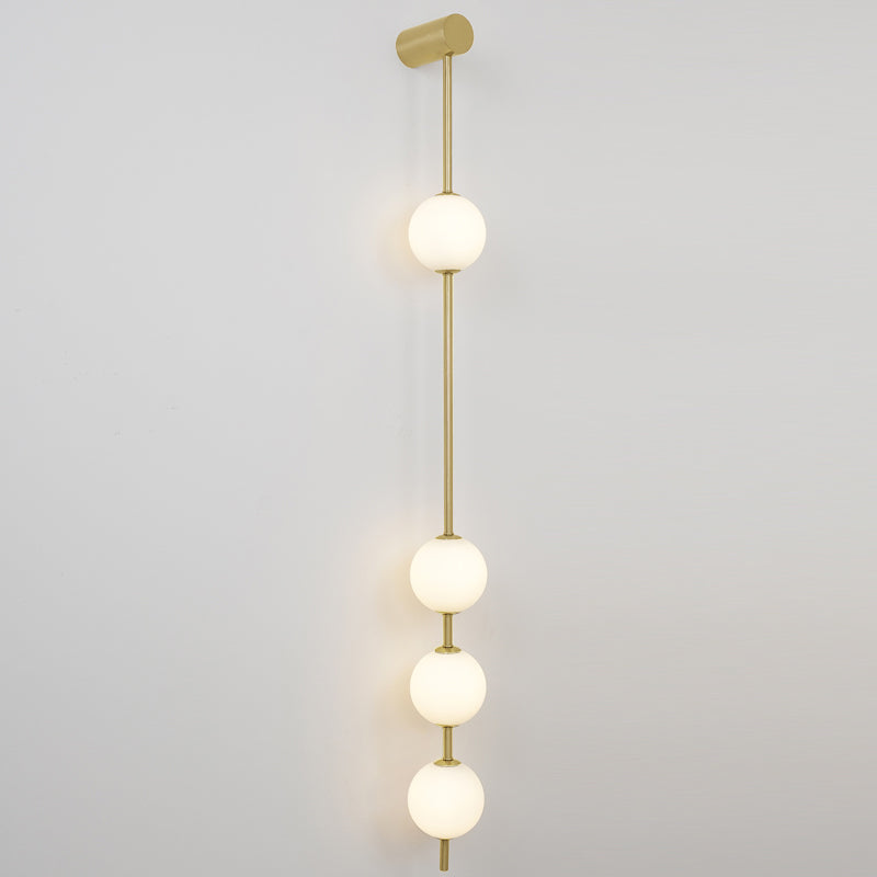 The Clérachic Stacked Globe Wall Sconce in brass, lit, four globes stacked in a straight vertical line on white.