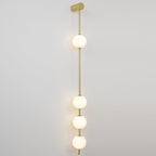 The Clérachic Stacked Globe Wall Sconce in brass, lit, four globes stacked in a straight vertical line on white.