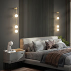 Two Clérachic Stacked Globe Wall Sconces in brass, lit, flanking a fluted headboard with three globes each.