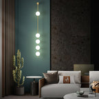 The Clérachic Stacked Globe Wall Sconce in brass, lit, five globes glowing on a teal wall beside a potted cactus.