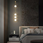 The Clérachic Stacked Globe Wall Sconce in brass, lit, four globes above a bedside table with candles.