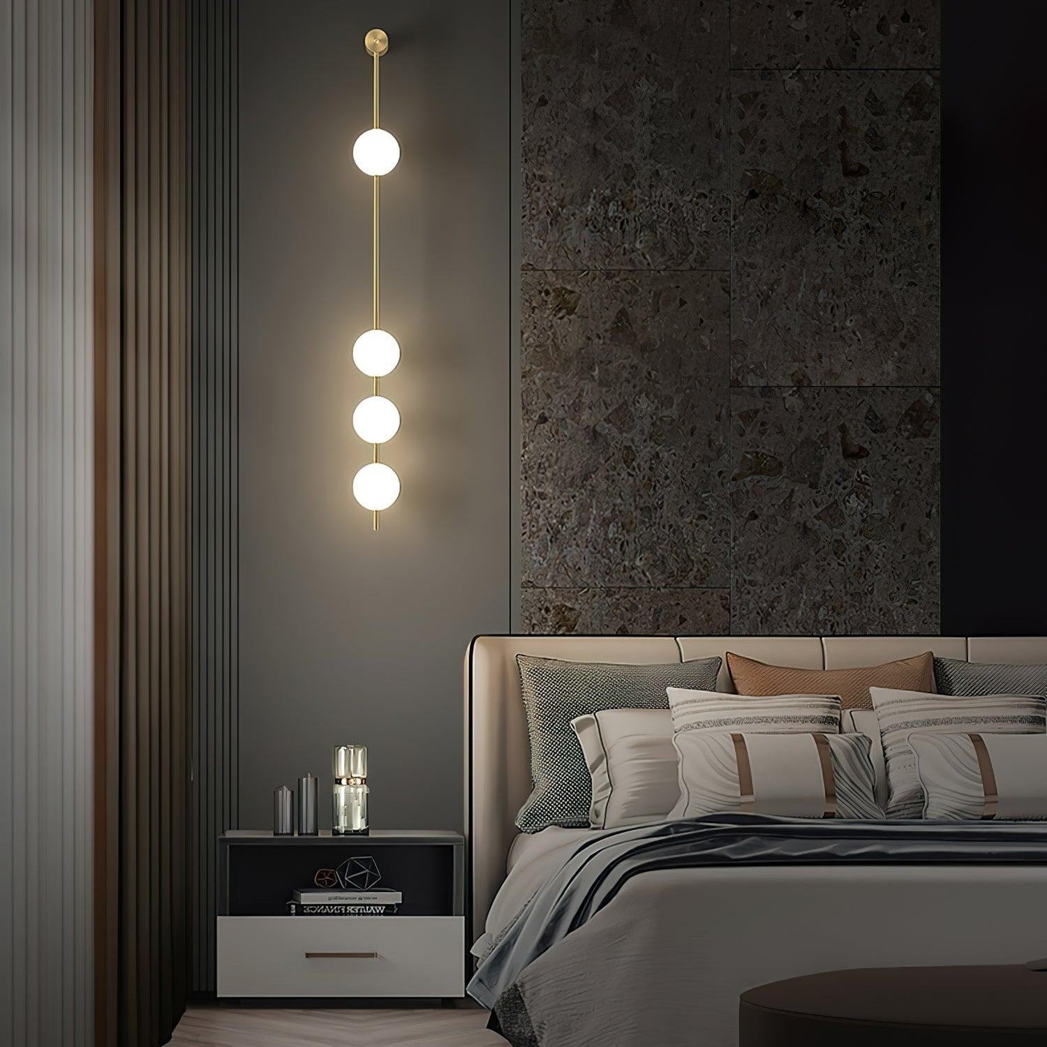 The Clérachic Stacked Globe Wall Sconce in brass, lit, four globes above a bedside table with candles.