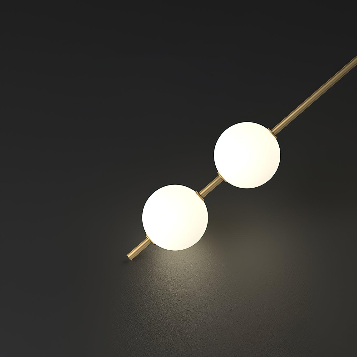 Close-up of the Clérachic Stacked Globe Wall Sconce in brass, two lit globes catching light on a dark floor.